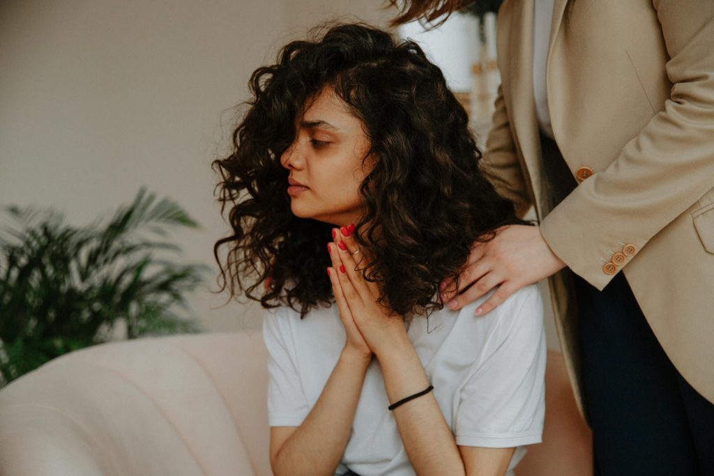 A young woman receives emotional support during a therapy session indoors.